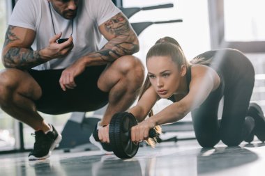 Zamanlayıcı ve genç sporcumuz abs rulo spor salonunda egzersiz yaparak ile oturan erkek kişisel antrenör