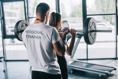 male personal trainer helping sportswoman to do exercises with barbell at gym clipart