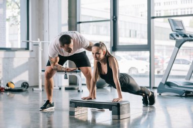male personal trainer helping sportswoman to do push ups at gym