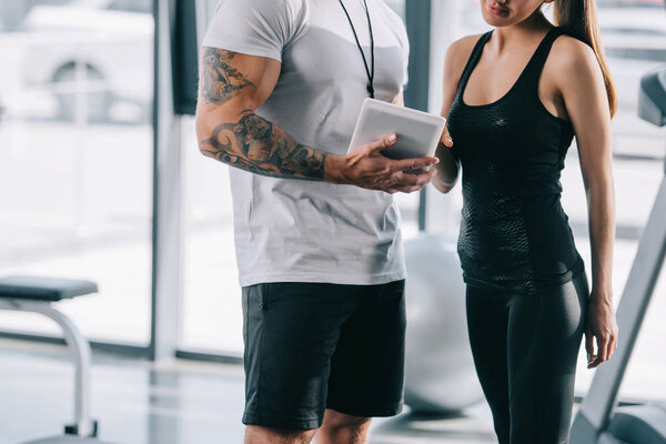 cropped image of male personal trainer showing schedule on digital tablet to sportswoman at gym 