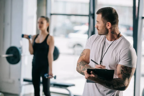 Male Personal Trainer Writing Clipboard Young Athletic Woman Exercising Dumbbells — Stock Photo, Image