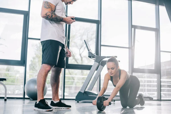 Male Personal Trainer Timer Young Sportswoman Doing Exercise Abs Roller — Stock Photo, Image