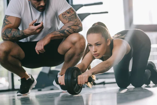 Mannelijke Persoonlijke Trainer Zitten Met Timer Jonge Sportvrouw Doen Oefening — Stockfoto