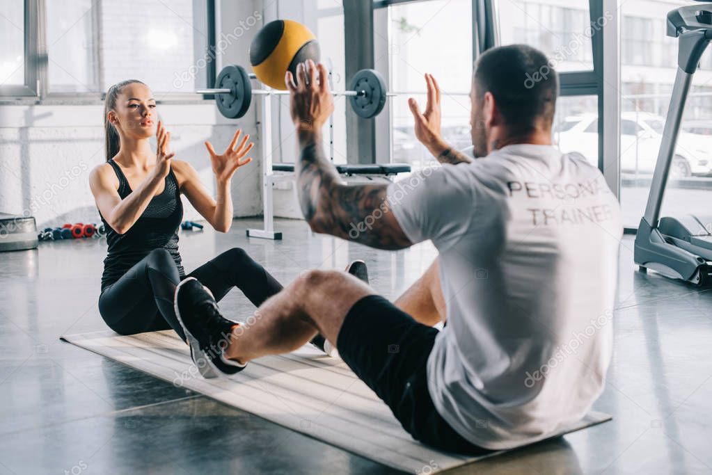 male personal trainer and sportswoman doing exercises with ball at gym