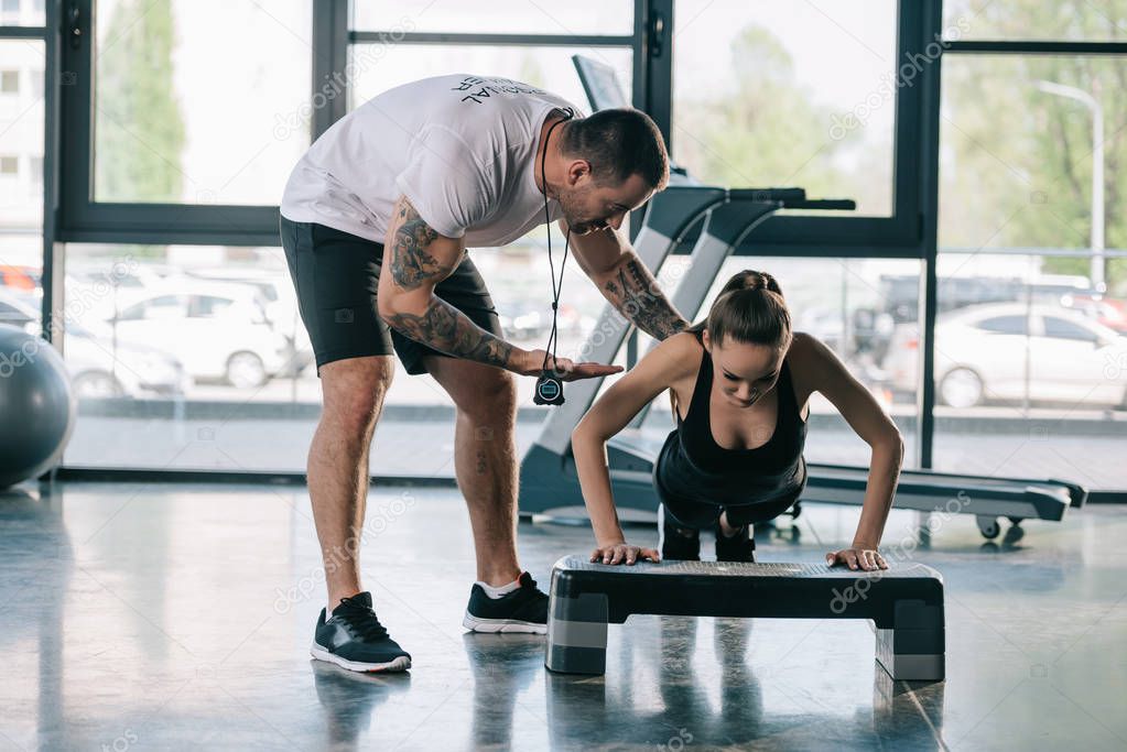 male personal trainer helping sportswoman to do push ups at gym