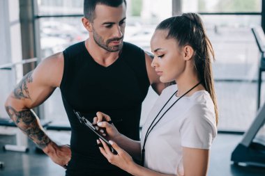 kadın kişisel antrenör Pano ve sporcu yakınındaki spor salonunda ayakta yazma