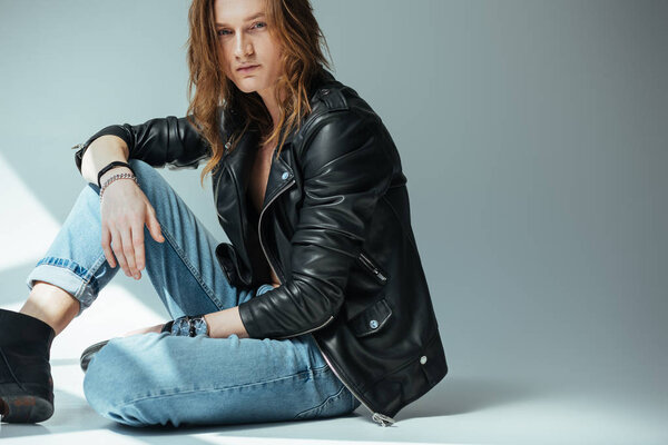 handsome man posing in jeans and black leather jacket, on grey