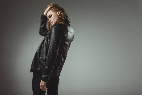 fashionable rocker with long hair posing in black leather jacket, isolated on grey