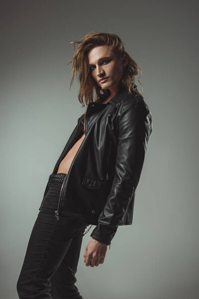 stylish man with long hair posing in black leather jacket, isolated on grey