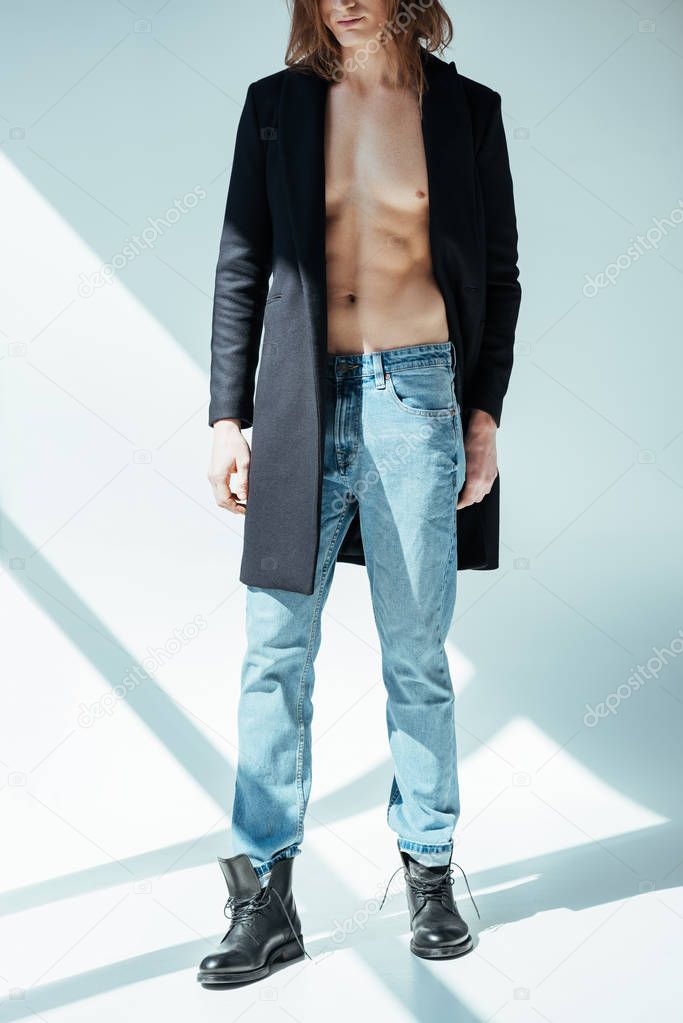 cropped view of elegant shirtless man posing in black jacket and jeans, on grey