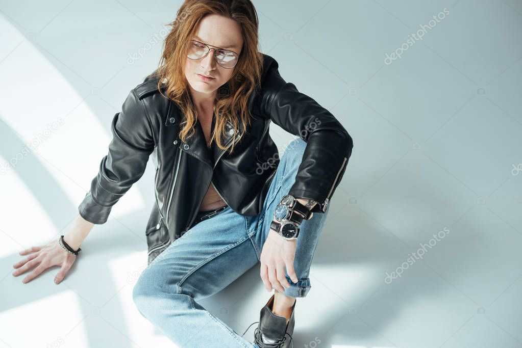 handsome male model posing in glasses, jeans and black leather jacket, on grey