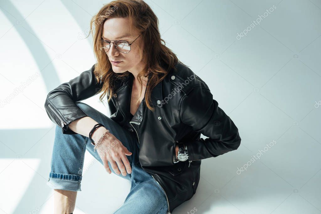 handsome stylish man posing in glasses, jeans and black leather jacket, on grey
