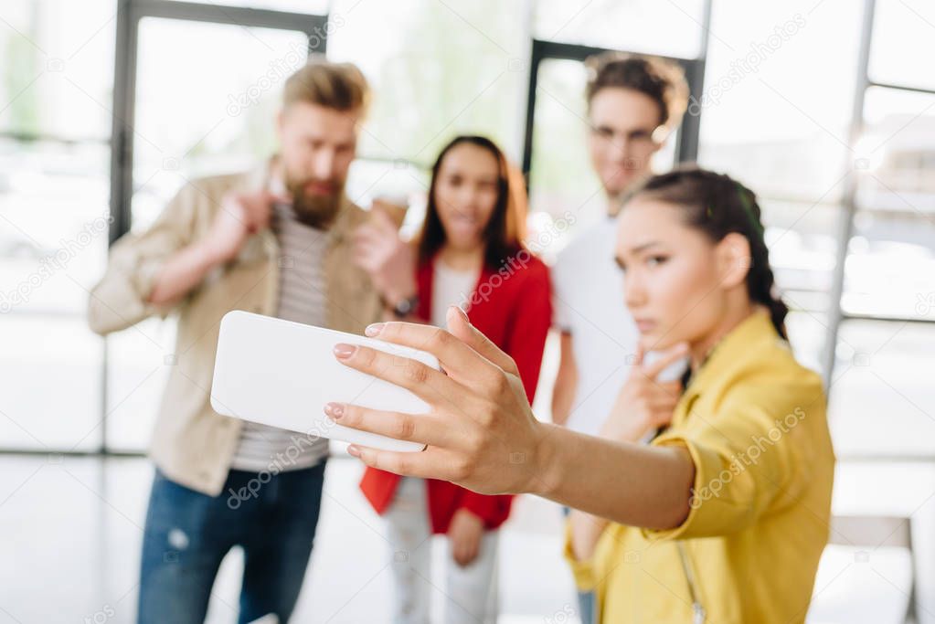Close-up view of smartphone in hand on woman taking selfie with her business team in modern office