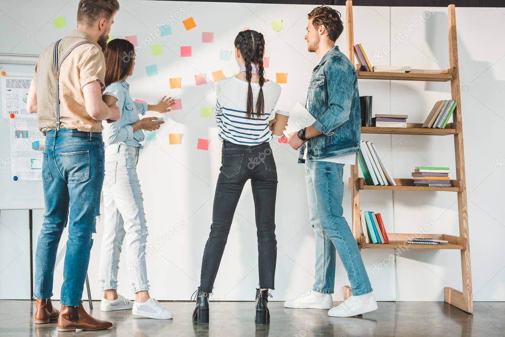 Professional business colleagues men and women looking at white board with sticky notes in modern office