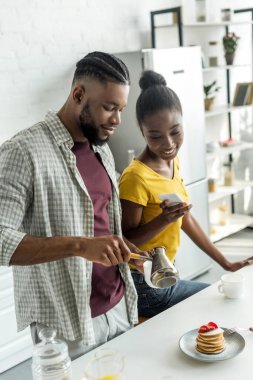 Afro-Amerikan kız arkadaşı alarak fotoğraf kahve ile smartphone mutfak at