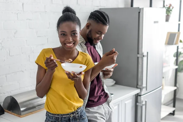 キッチンで朝食を持っているアフリカ系アメリカ人のカップルの笑顔  — 無料ストックフォト