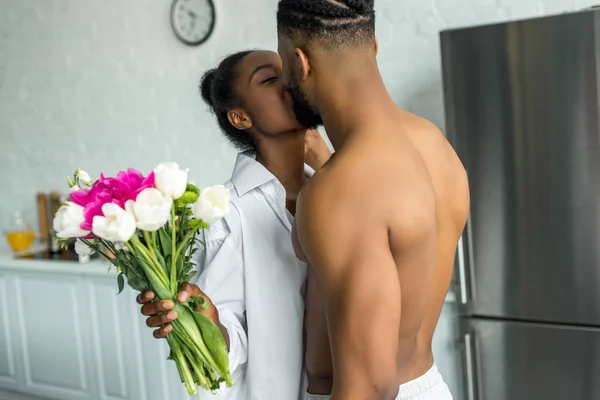 African American Couple Kissing Girlfriend Holding Bouquet Kitchen — Stock Photo, Image