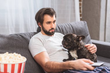 oturma odasında kanepede bulldog ile TV izlerken yalnız adam 