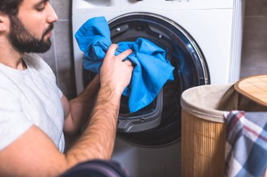 side view of loner putting laundry in washing machine in bathroom