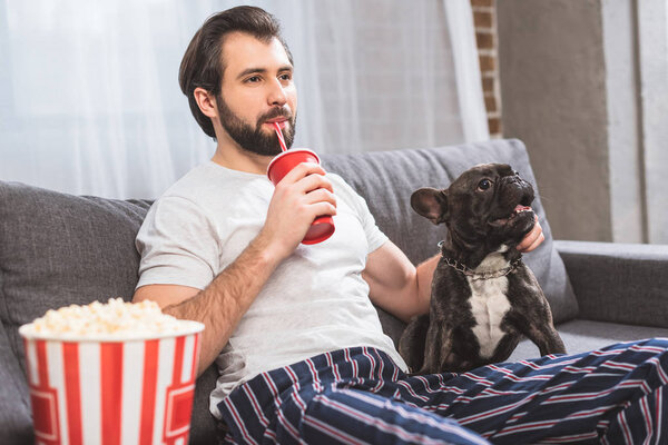 handsome loner palming bulldog and drinking beverage on sofa at home
