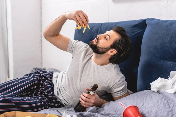 Przystojny Samotnikiem Jeść Frytki Trzymając Butelkę Piwa Sypialni — Zdjęcie stockowe