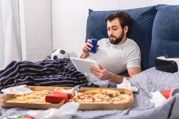 handsome loner using tablet and holding drink on bed in bedroom