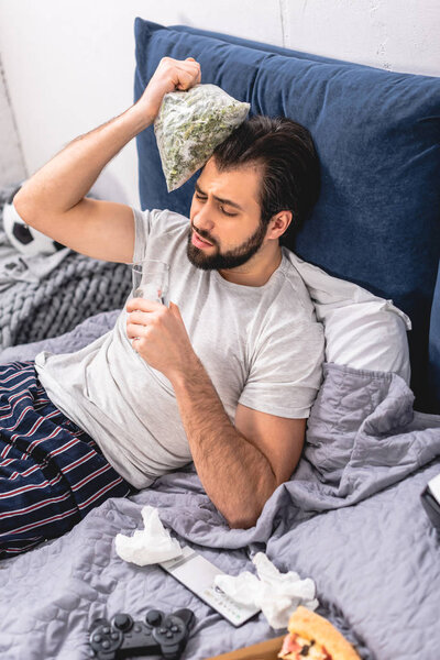 loner having headache with hangover and touching head with frozen green beans in bedroom