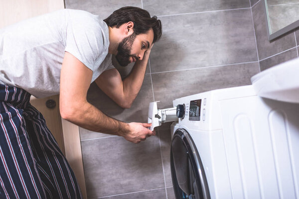 side view of handsome loner looking at washing machine in bathroom