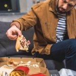Cropped image of angry loner taking piece of pizza at living room