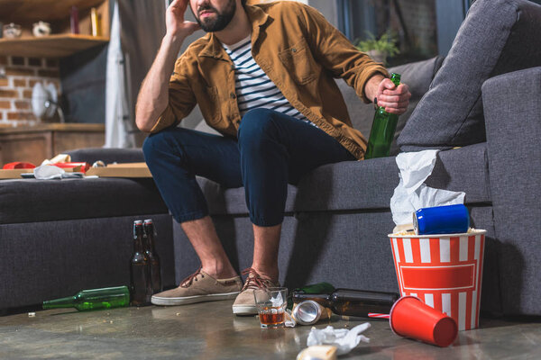 cropped image of loner holding bottle of alcohol drink at living room