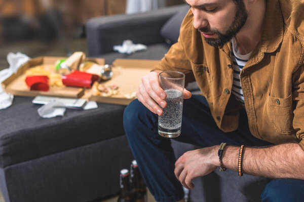 loner with hangover holding glass of water at living room