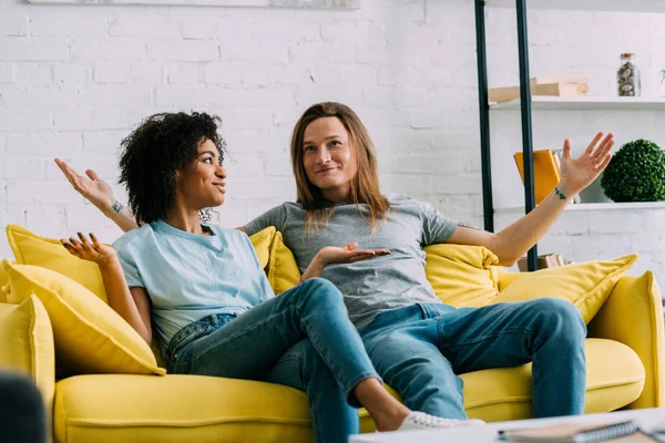 Pasangan Tersenyum Multietnis Dengan Tangan Lebar Duduk Sofa Rumah — Stok Foto