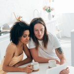 Ung man med tatuerade hand sitter med flickvän och använder digital tablett på köksbordet