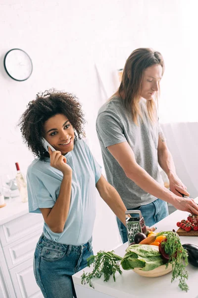 アフリカ系アメリカ人女性の切断彼女の彼氏のチェリー トマト キッチンで中のスマート フォンの話を笑ってください  — 無料ストックフォト