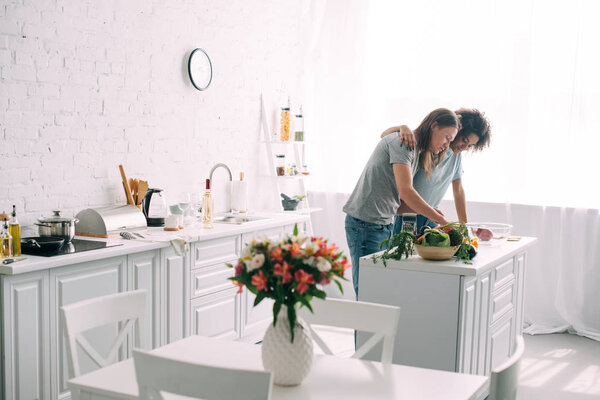 front view of young african american woman embracing boyfriend while he cooking at kitchen 
