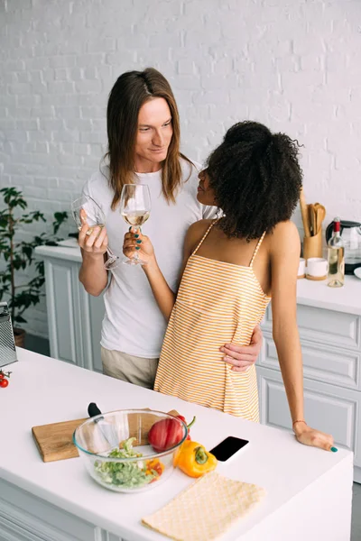 Young Man Embracing African American Woman Holding Wine Glass Kitchen — Free Stock Photo