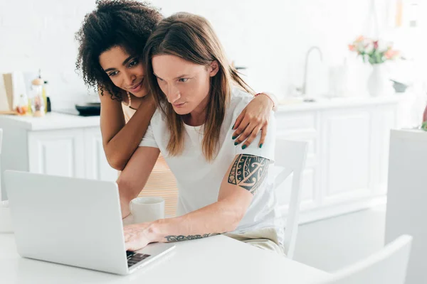 Young Man Tattooed Hand Typing Laptop Girlfriend Embracing Him — Stock Photo, Image