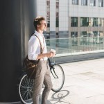 Stylish young man with coffee to go and vintage bicycle on rooftop of business building