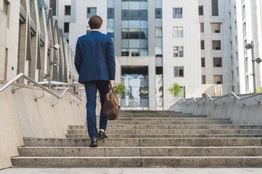 rear view of businessman in stylish suit with leather briefcase going up stairs clipart