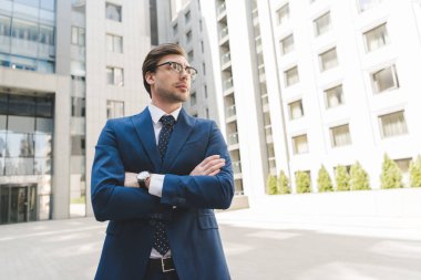 Alt görünümü çapraz kollu şık elbiseli ciddi genç işadamı