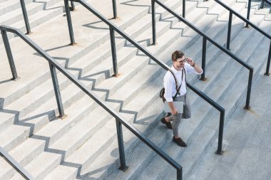 high angle view of stylish young man walking on stairs with laptop on city street clipart