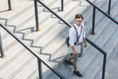 high angle view of handsome young man walking on stairs with laptop on city street clipart