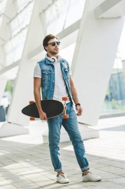 denim giysileri longboard ve kulaklık ile genç kaykaycı
