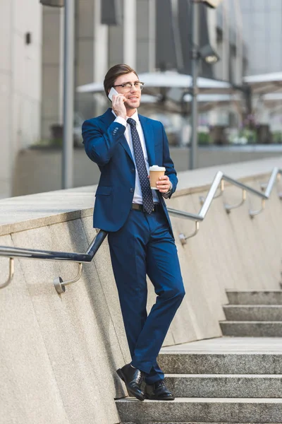 成功的年轻商人在时髦的西装与咖啡去谈电话在楼梯附近的商业大厦 — 图库照片