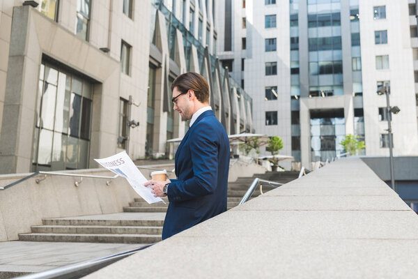 handsome young businessman with coffee to go reading newspaper