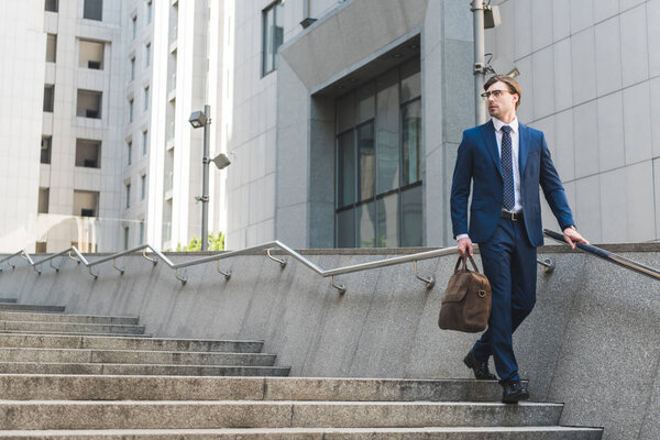 attractive young businessman in stylish suit with briefcase in business district