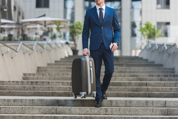 cropped shot of businessman with luggage and flight tickets going down stairs in business district