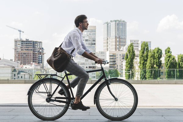 side view of young man in stylish clothes riding vintage bicycle on city street