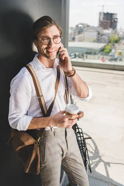 smiling young man with coffee to go talking by phone