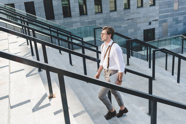 handsome young man walking on stairs with laptop on city street